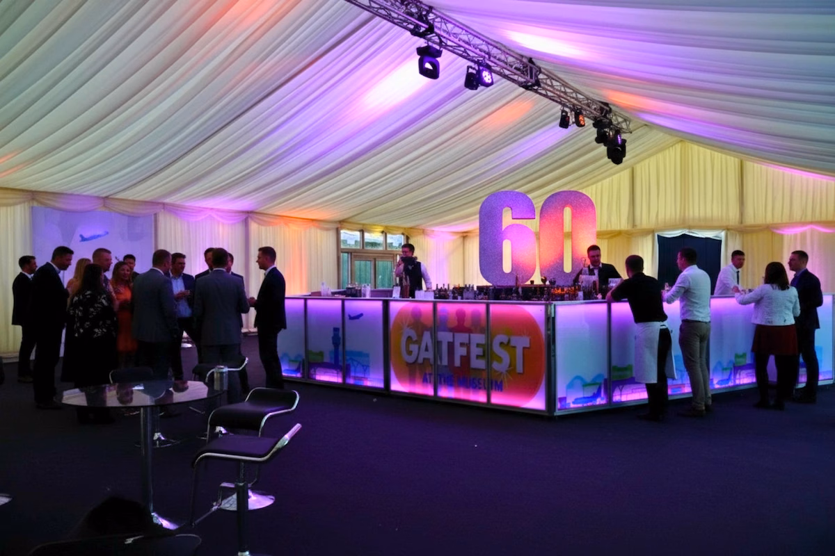 Large 9-metre illuminated pink LED centerpiece bar with guests mingling at a corporate marquee activation.