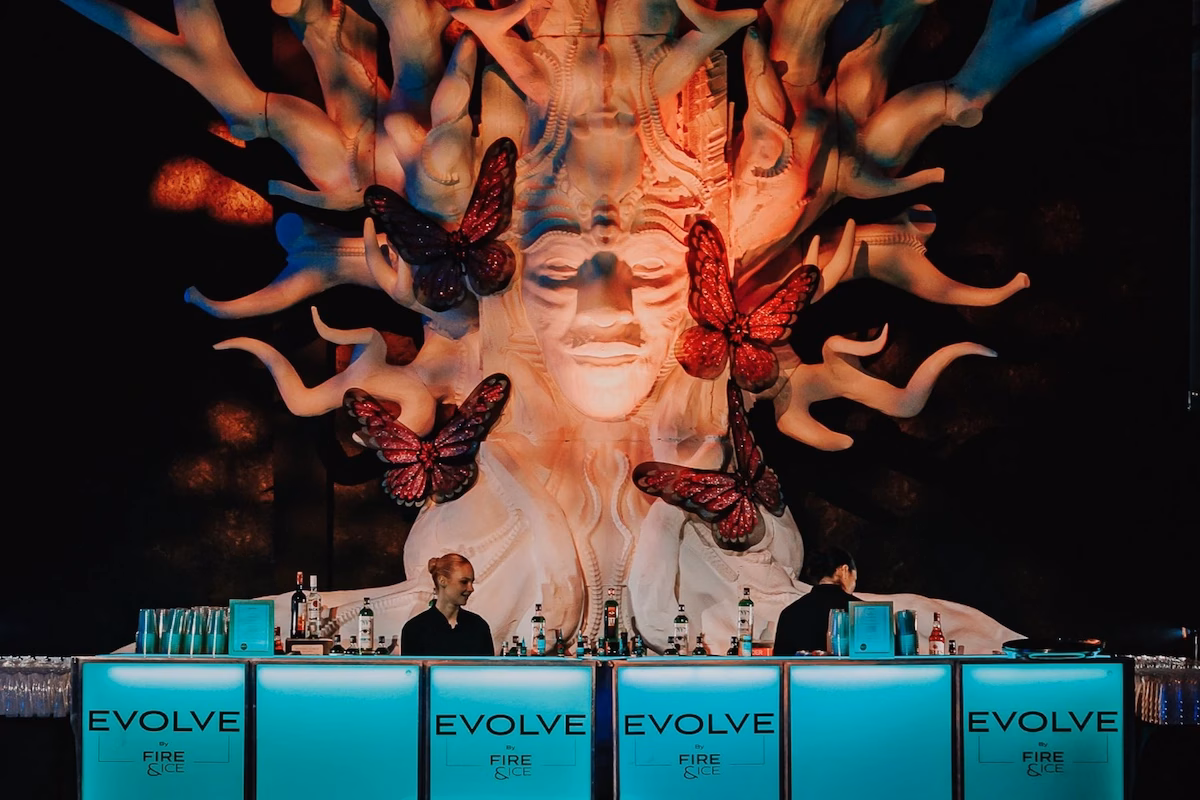 Custom branded EVOLVE mobile bar with teal LED illumination and dramatic theatrical backdrop at a corporate brand activation.